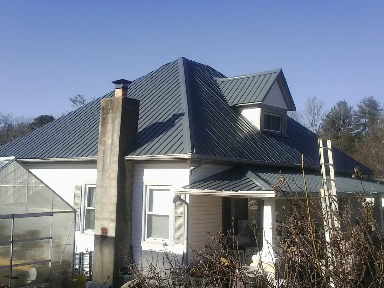 Dark blue standing seam metal roof on a white farmhouse with dormer — Slate & Tile Roof Repair by Roofing Brothers in Canon City
