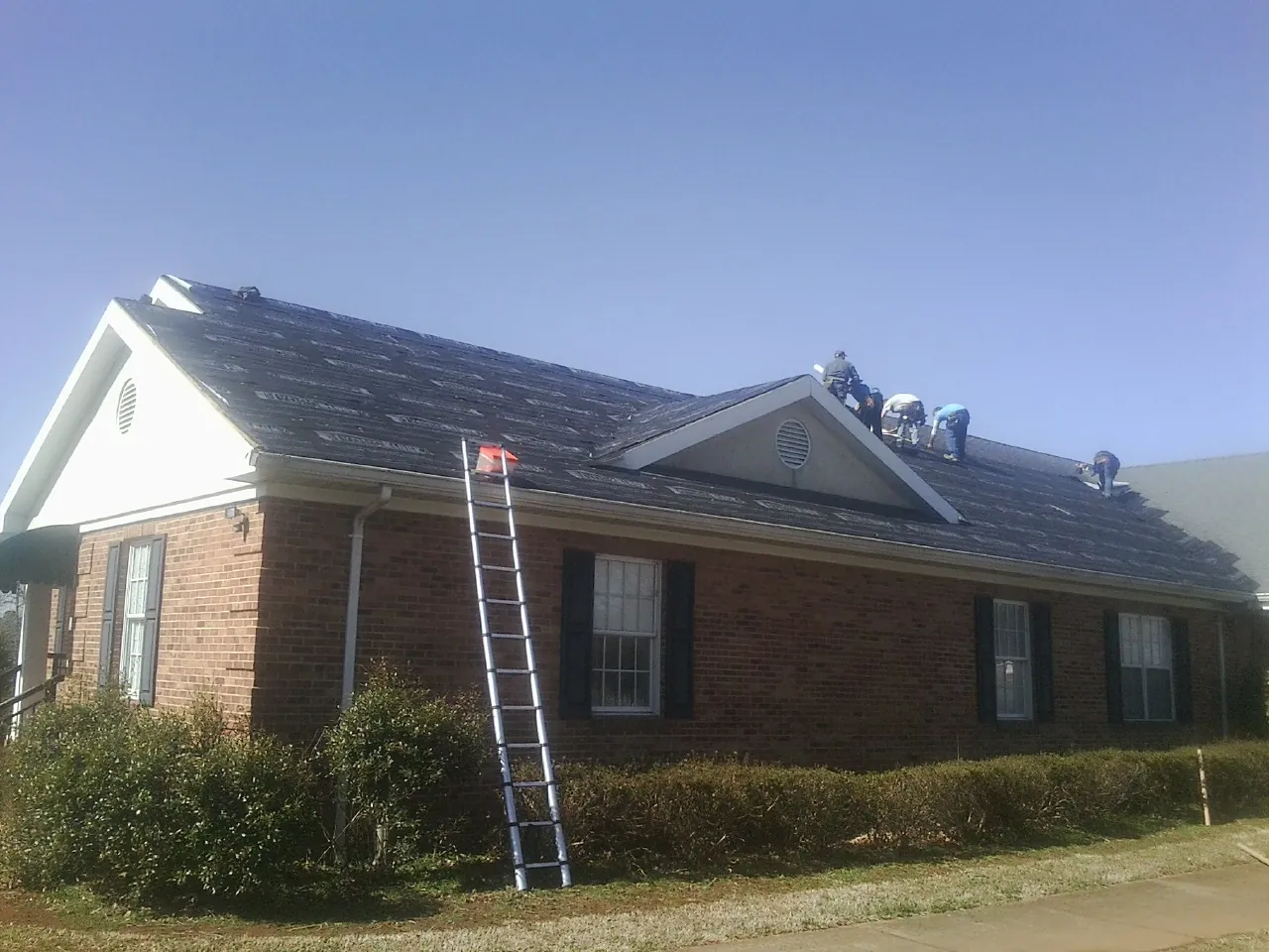 Crew tearing shingles off a brick ranch roof with a ladder set — Emergency Roof Repair work by our crew in Canon City