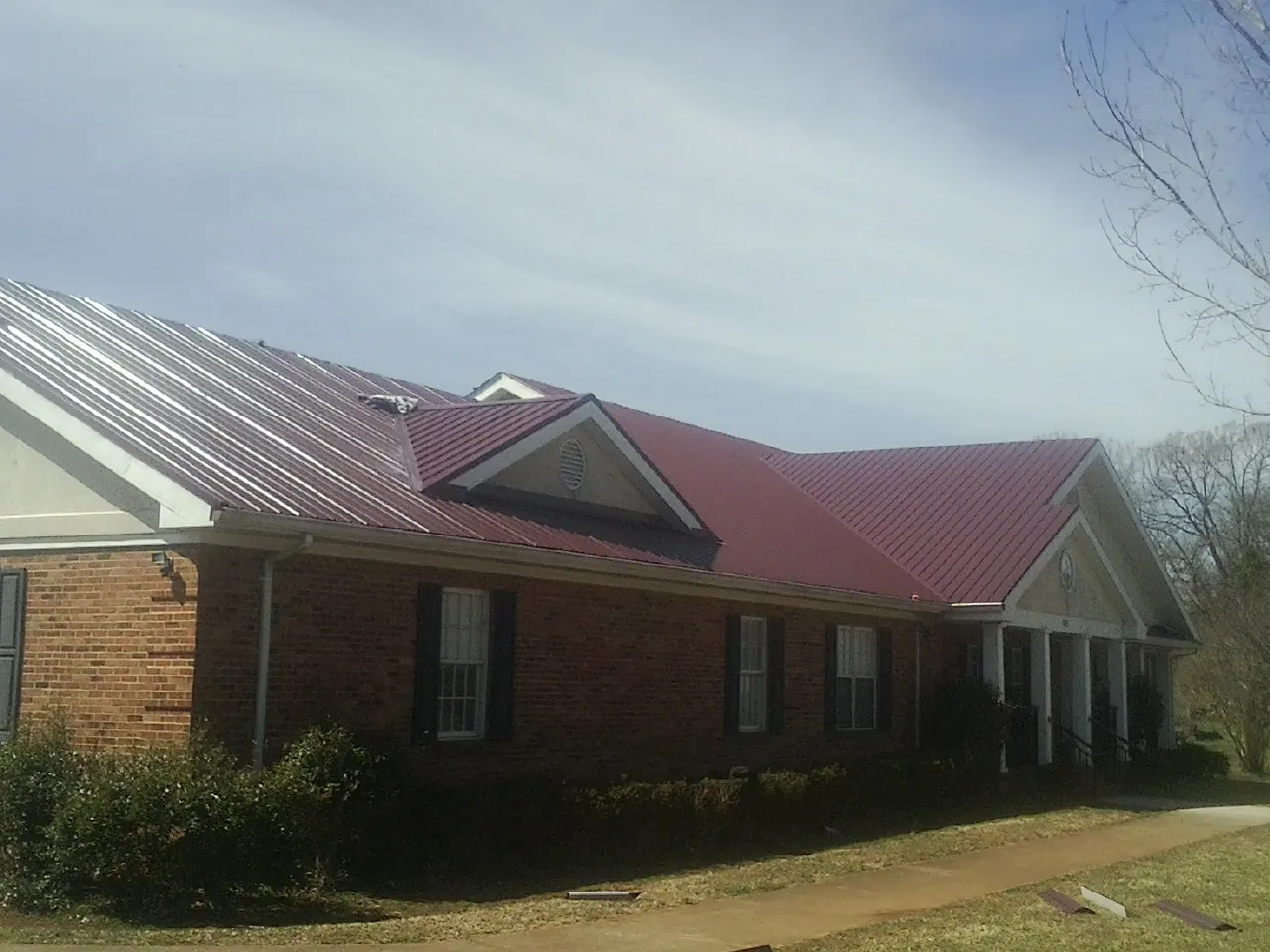 Red metal roof with gabled entries on a long brick building, from a Hail Damage Roof Repair job in Canon City