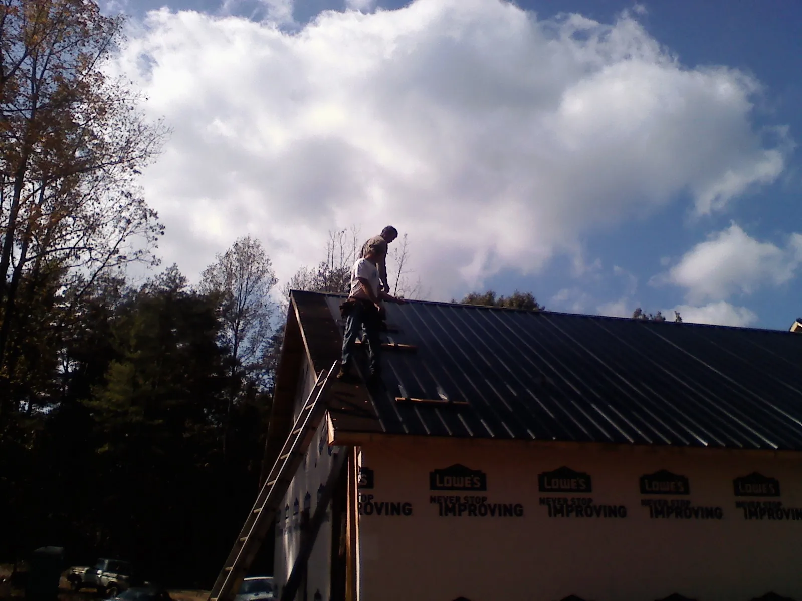 Roofer fastening dark metal panels high against a cloudy sky, from a Roof Inspection job in Canon City