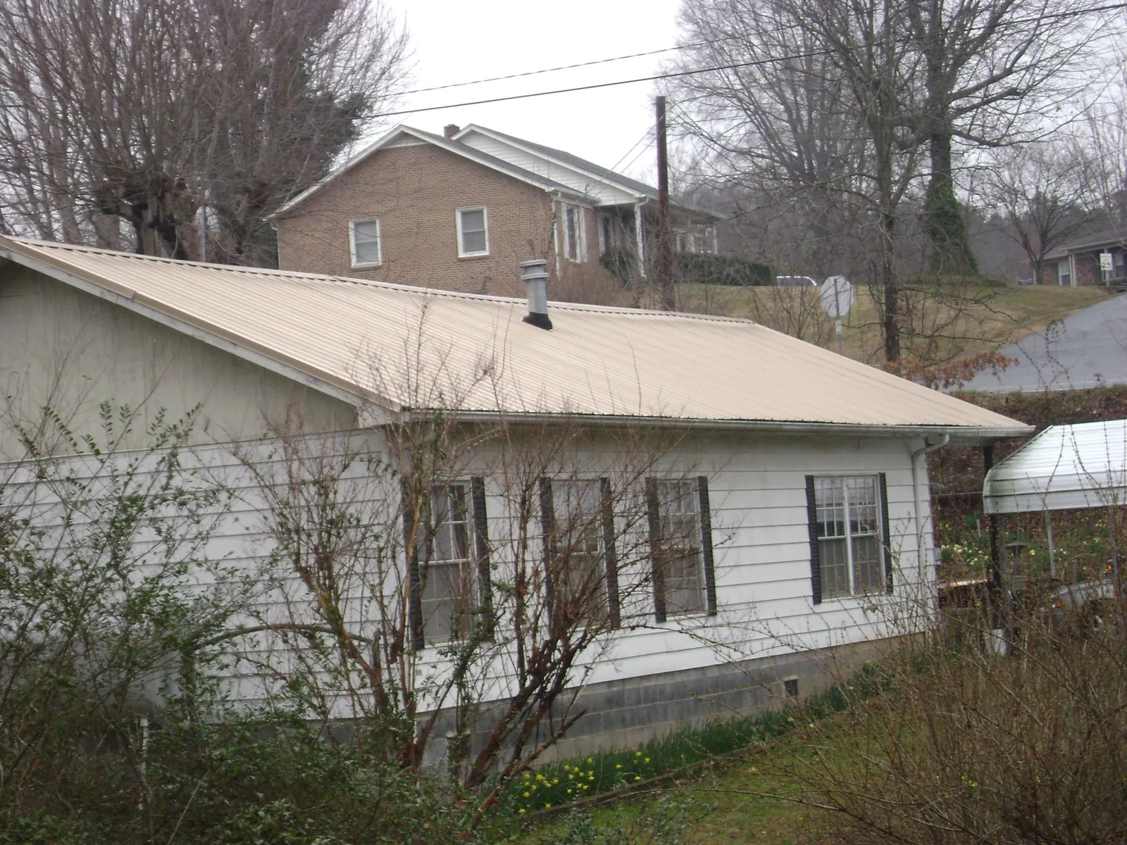Tan metal roof on a white sided house set into a hillside — Commercial Roofing by Roofing Brothers in Canon City